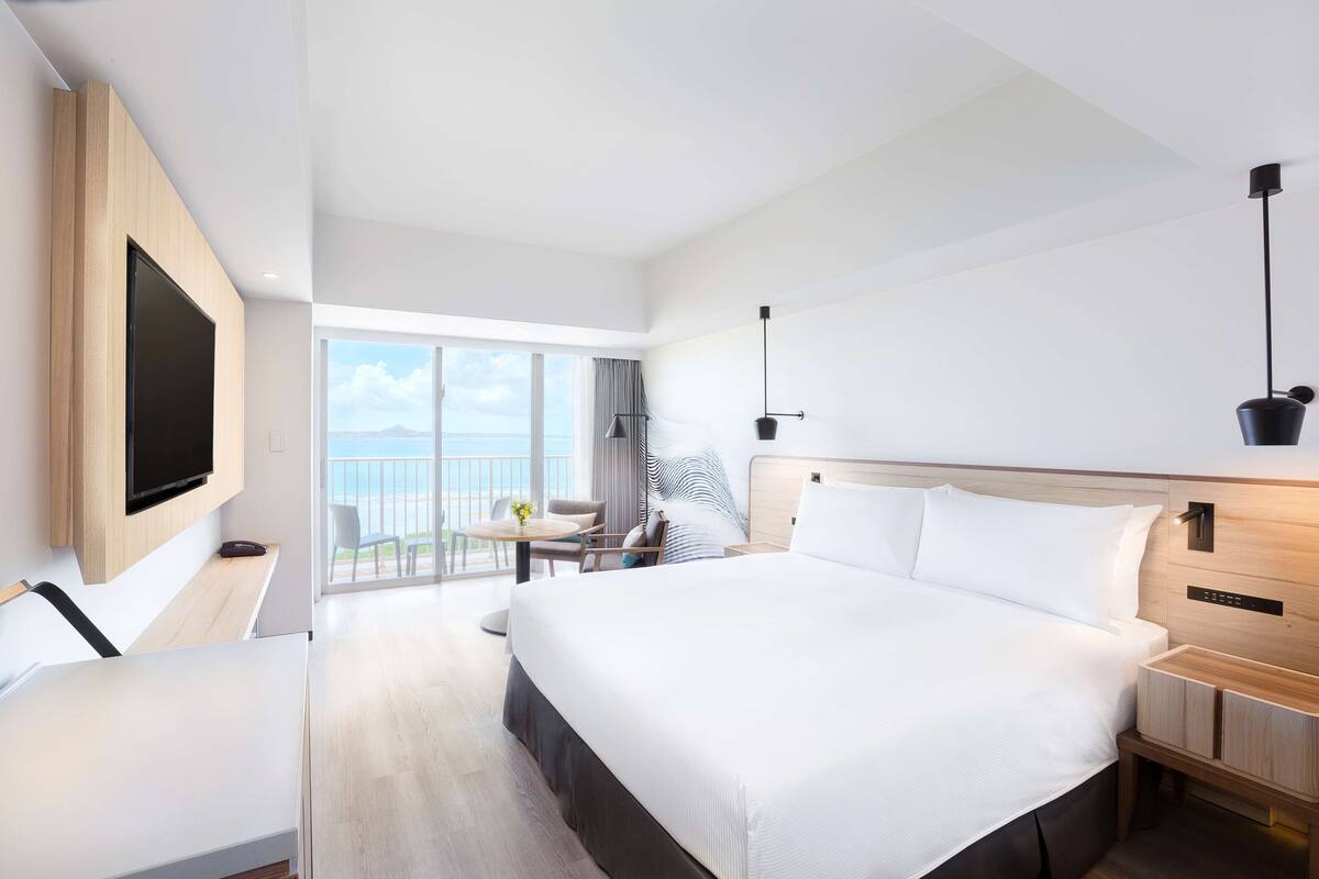 Habitación de hotel moderna con una cama grande, un escritorio, un televisor y un balcón con vistas.