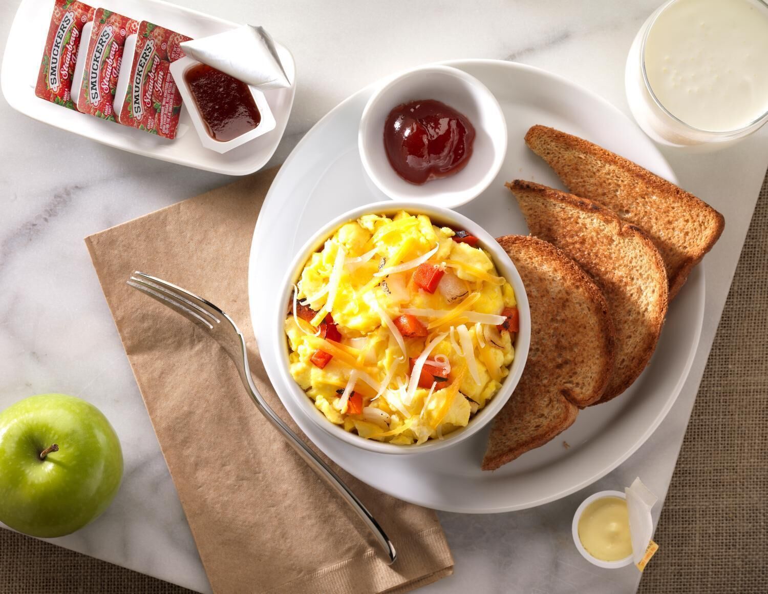 A breakfast plate with scrambled eggs, toast, jam, and butter.