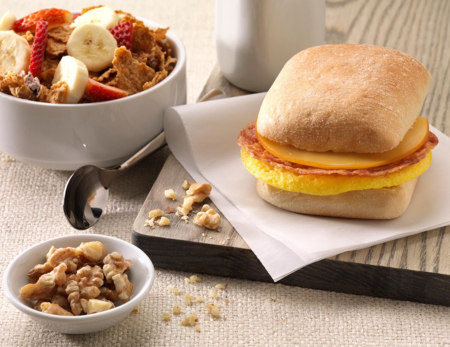 Una escena de desayuno con un sándwich, un tazón de cereal y un cuenco pequeño de nueces.