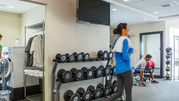 A gym with a washing machine, a rack of dumbbells, and a spinning bike.