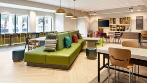 A modern lounge area with a green sofa, wooden chairs, a dining table, and pendant lighting. - Home2 Suites by Hilton Stuart (Stuart)