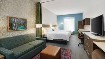 A hotel room with a green sofa, two beds, a TV, and a desk.