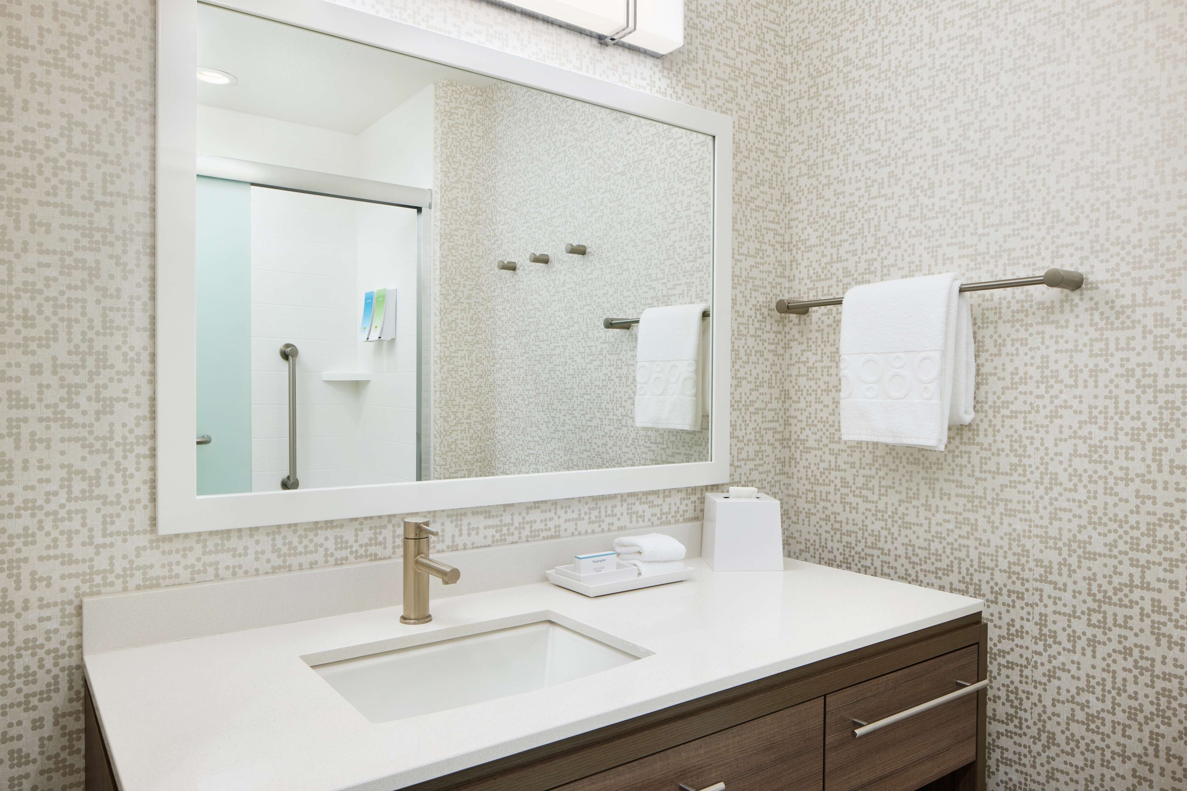 A modern bathroom with a large mirror, a sink, a towel rack, and a toilet paper dispenser.