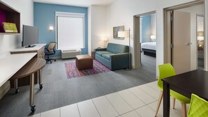A hotel room with a desk, chair, couch, and a bed. - Home2 Suites by Hilton Stuart (Stuart)