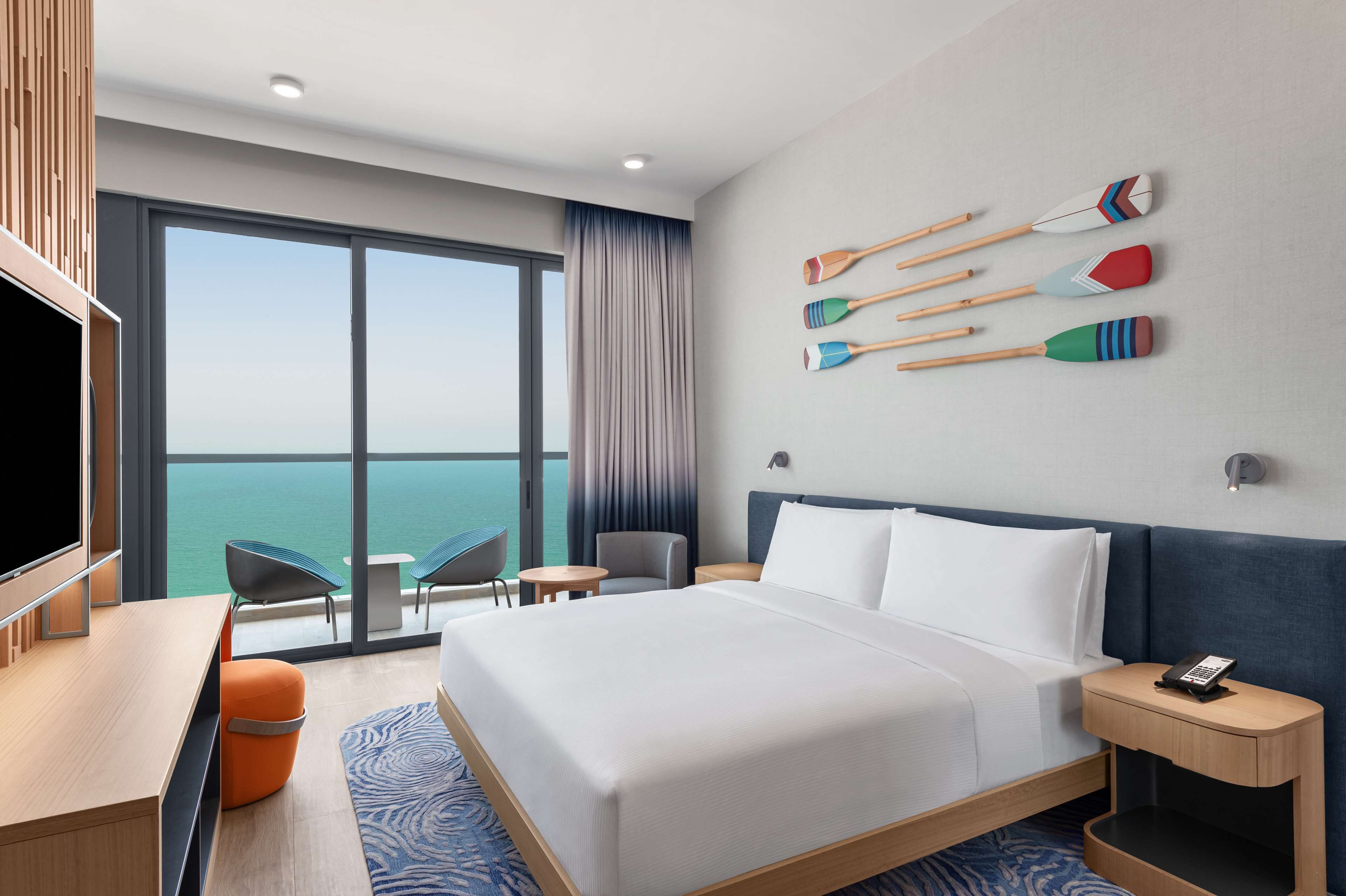 Une chambre d’hôtel avec un grand lit, un bureau, une télévision, une vue sur l’océan et un mur décoré de planches de surf.