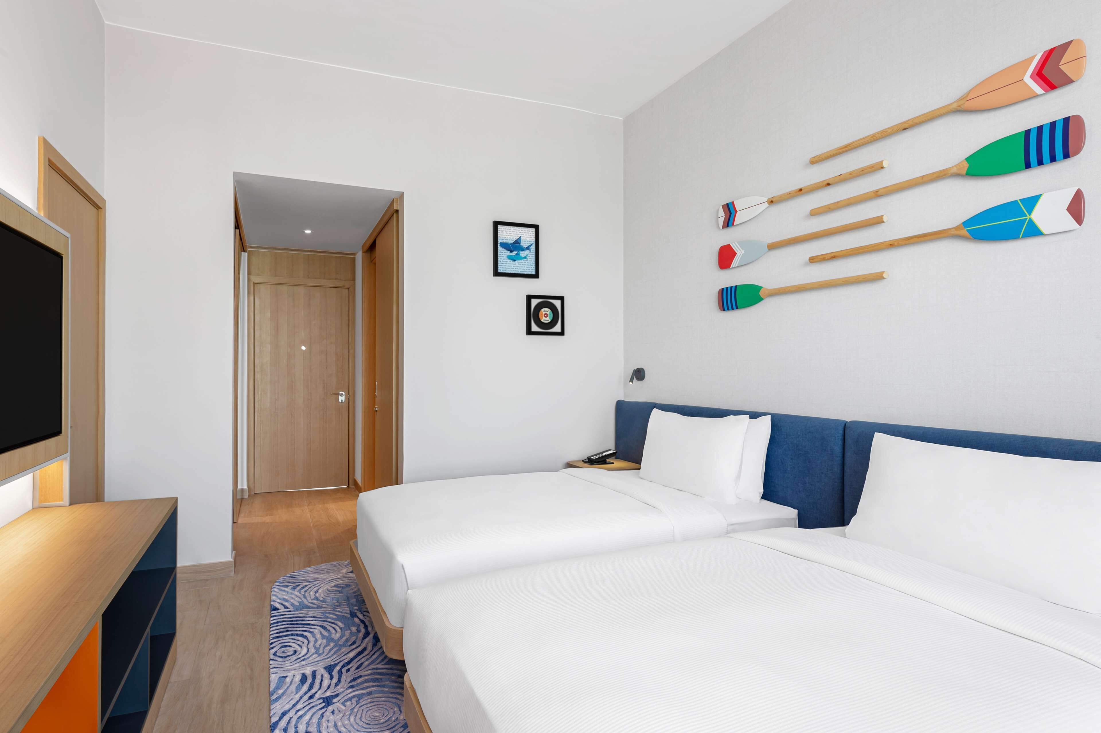 A hotel room with two beds, a TV, and a wall decorated with colorful paddleboards.