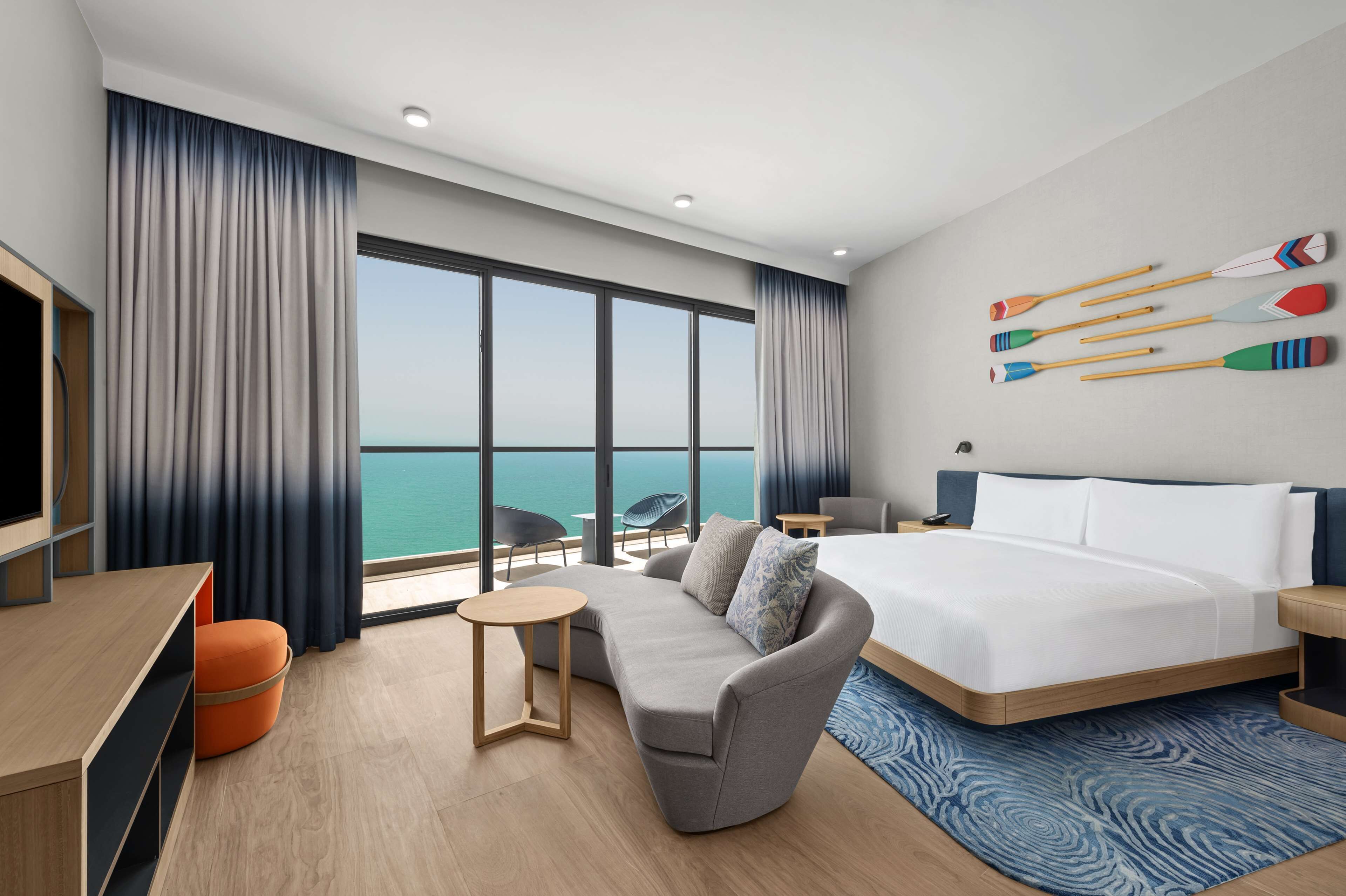 Een moderne hotelkamer met een groot bed, een bank, een televisie en uitzicht op zee.