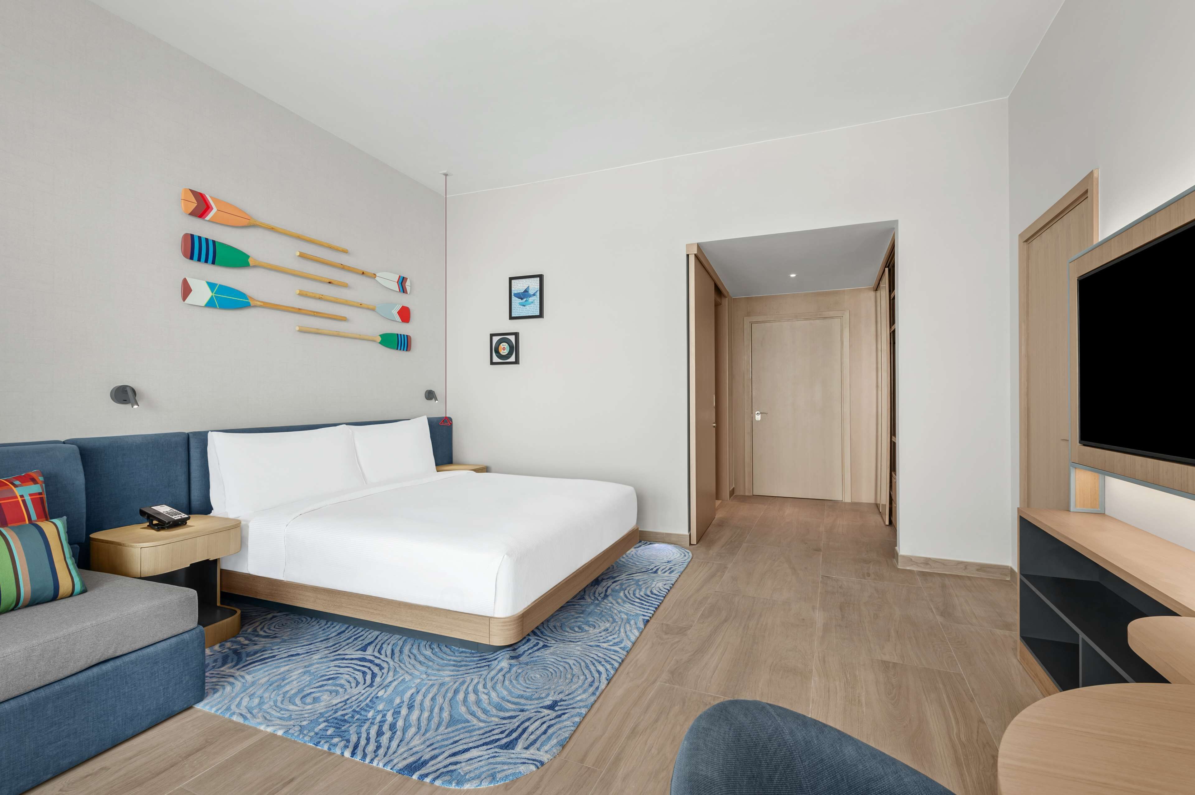 Ett modernt hotellrum med en säng, en soffa, en tv och en vägg med dekorativa föremål.