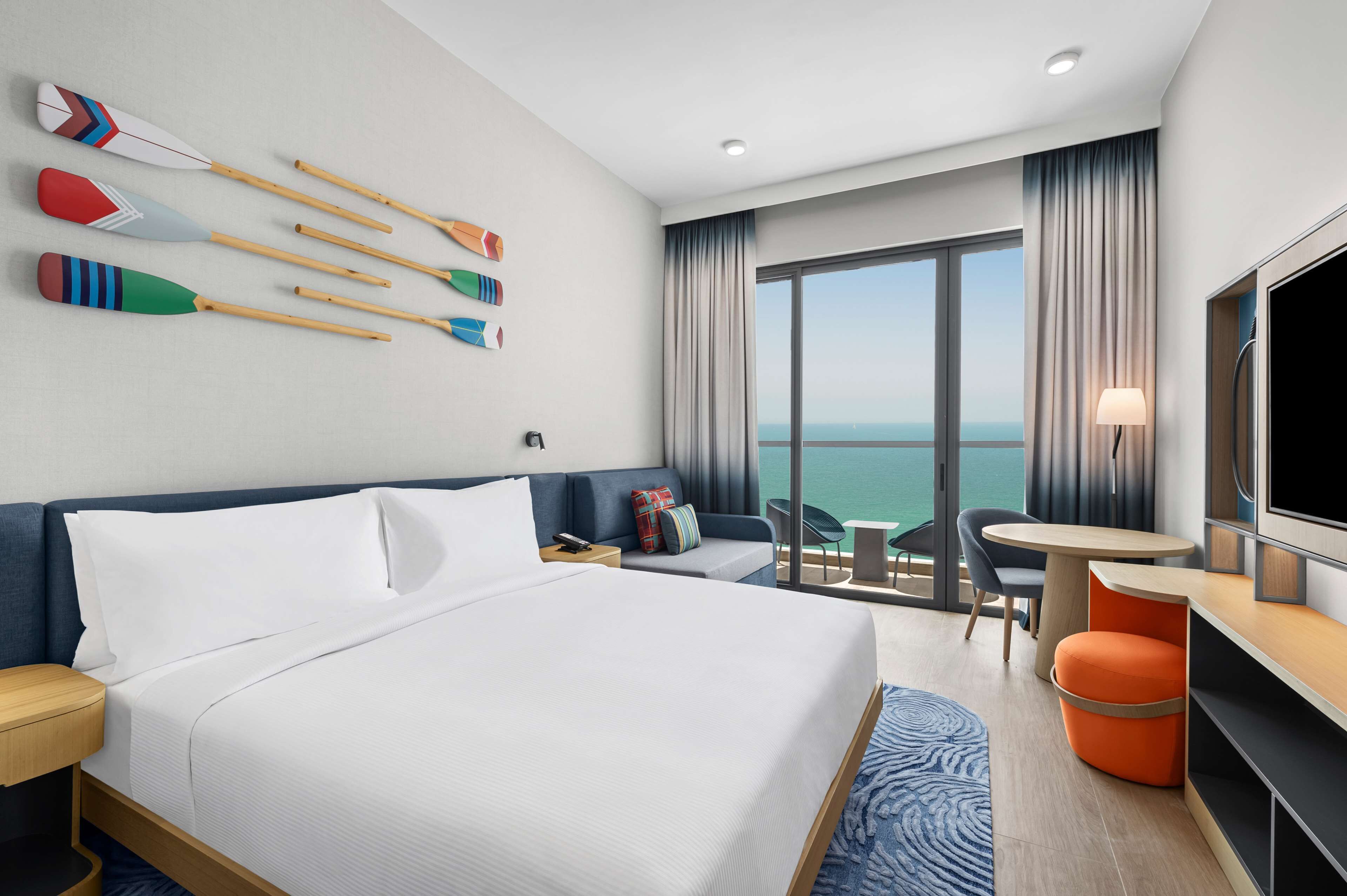 A hotel room with a large bed, a TV, a balcony with a view of the sea, and several decorative paddles on the wall.