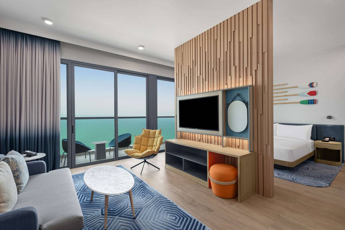 Ein modernes Hotelzimmer mit großem Balkon, Fernseher, Bett und einer Sitzecke mit Meerblick.
