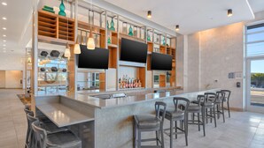 Een moderne bar met een lange toonbank, diverse barkrukken en een ruim assortiment flessen.