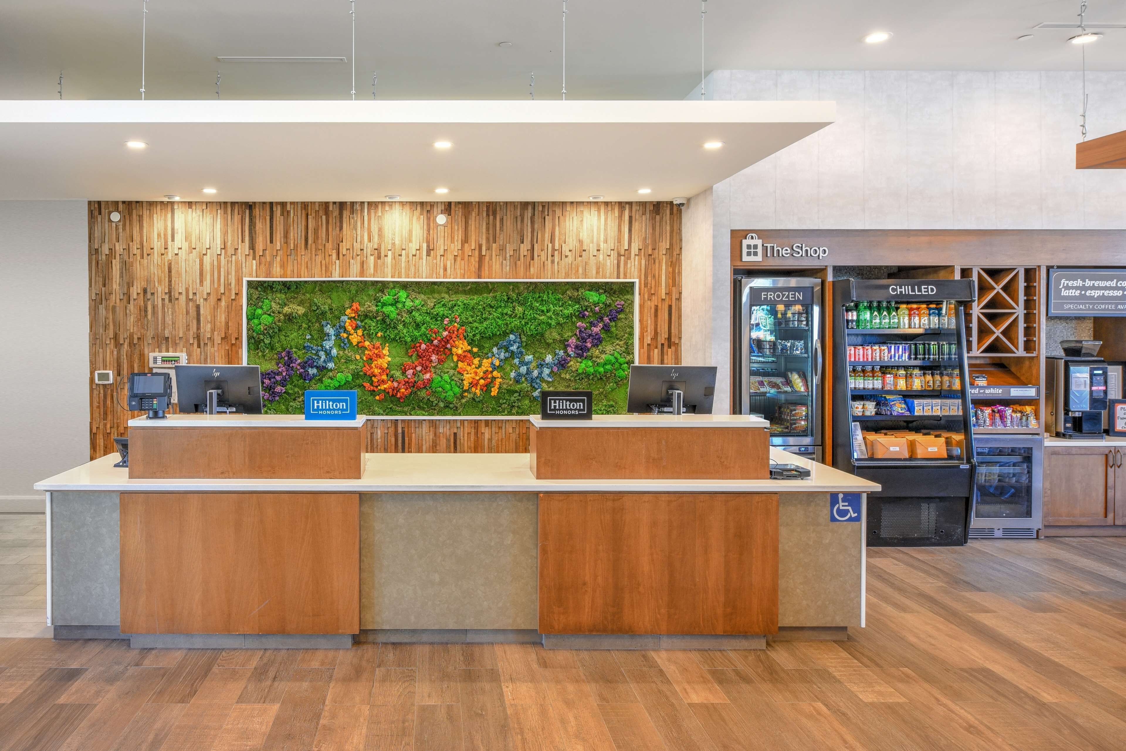 A hotel reception desk with a wooden finish, a digital display, and a wall-mounted floral art piece.