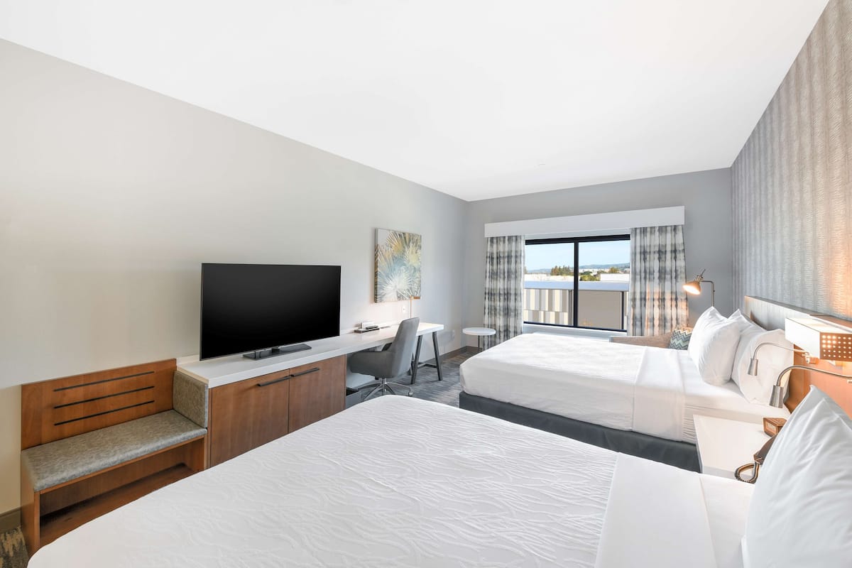 A hotel room with two beds, a desk, a TV, and a window with curtains.