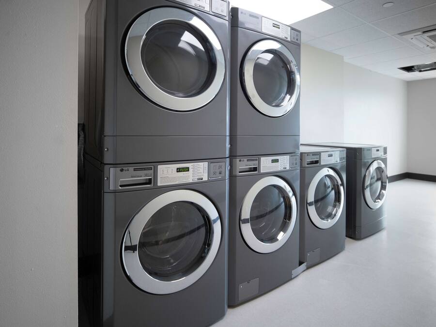 A row of four stacked front-loading washing machines in a commercial laundry room.
