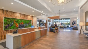 Een moderne receptie met een houten balie, een groene wand met kleurrijke planten en een zithoek met uitzicht op het omliggende landschap.