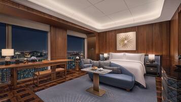 A modern hotel room with a large bed, a desk with a lamp, a sofa, and a view of the city at night.