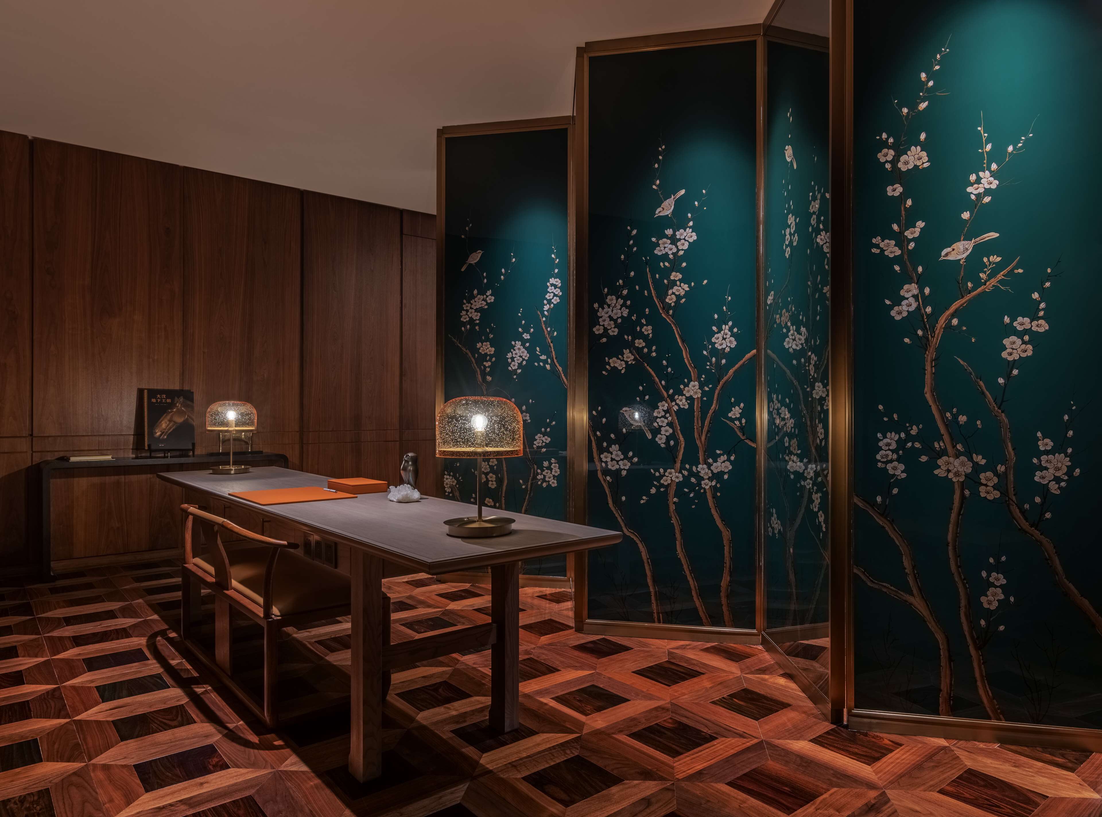 Une pièce avec un bureau en bois, deux lampes et un mur décoratif orné de motifs floraux.