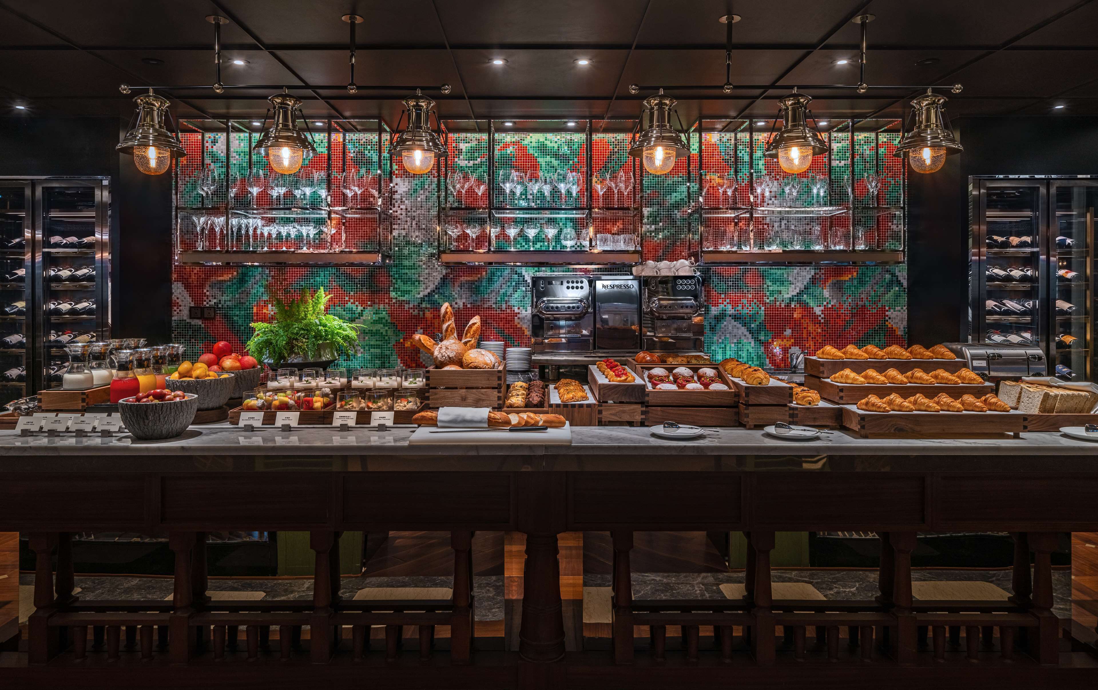 A breakfast buffet with various food items, a coffee machine, and a decorative wall with a mosaic pattern.