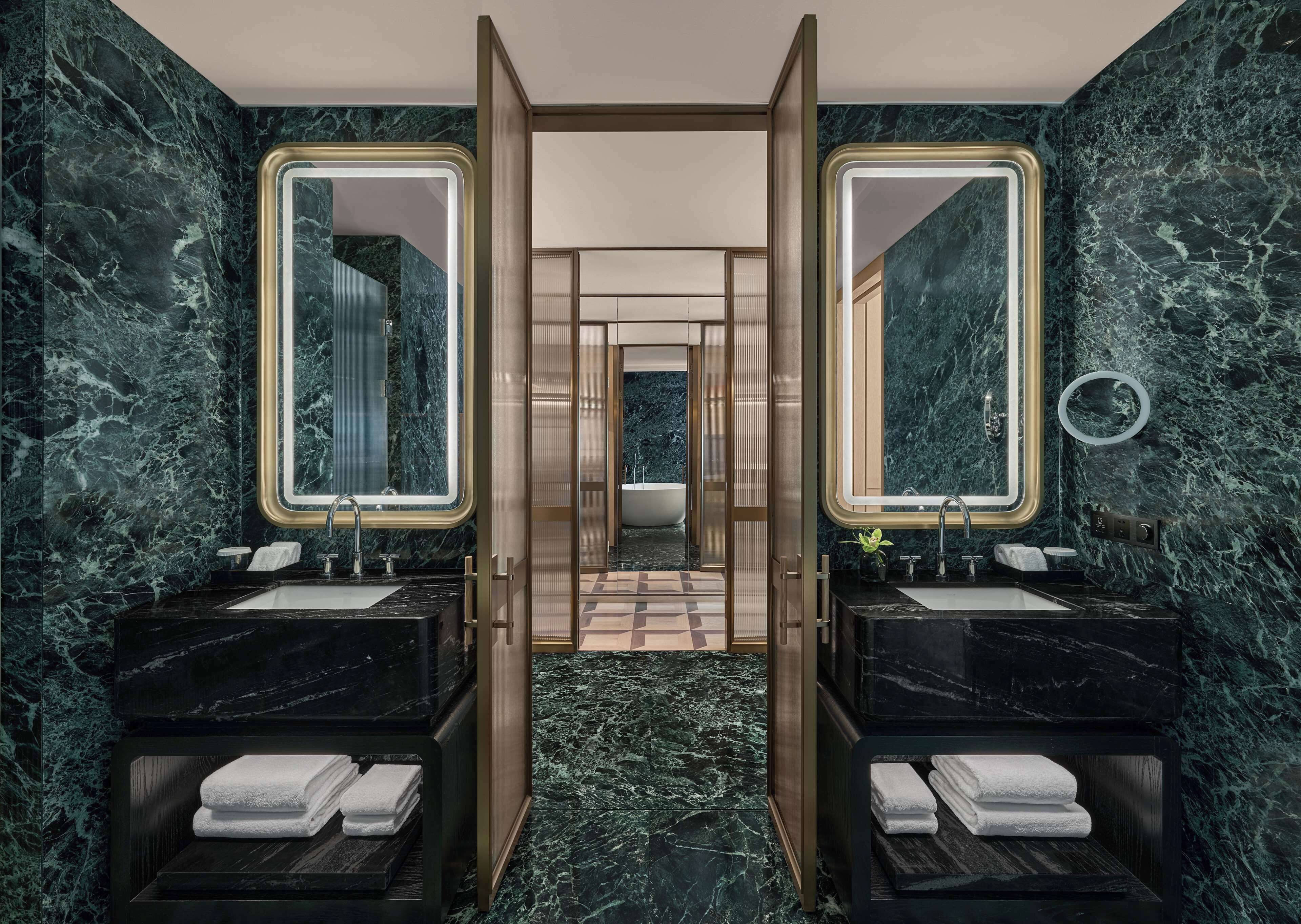 Un baño lujoso con dos lavamanos de mármol, espejos grandes y acceso central.