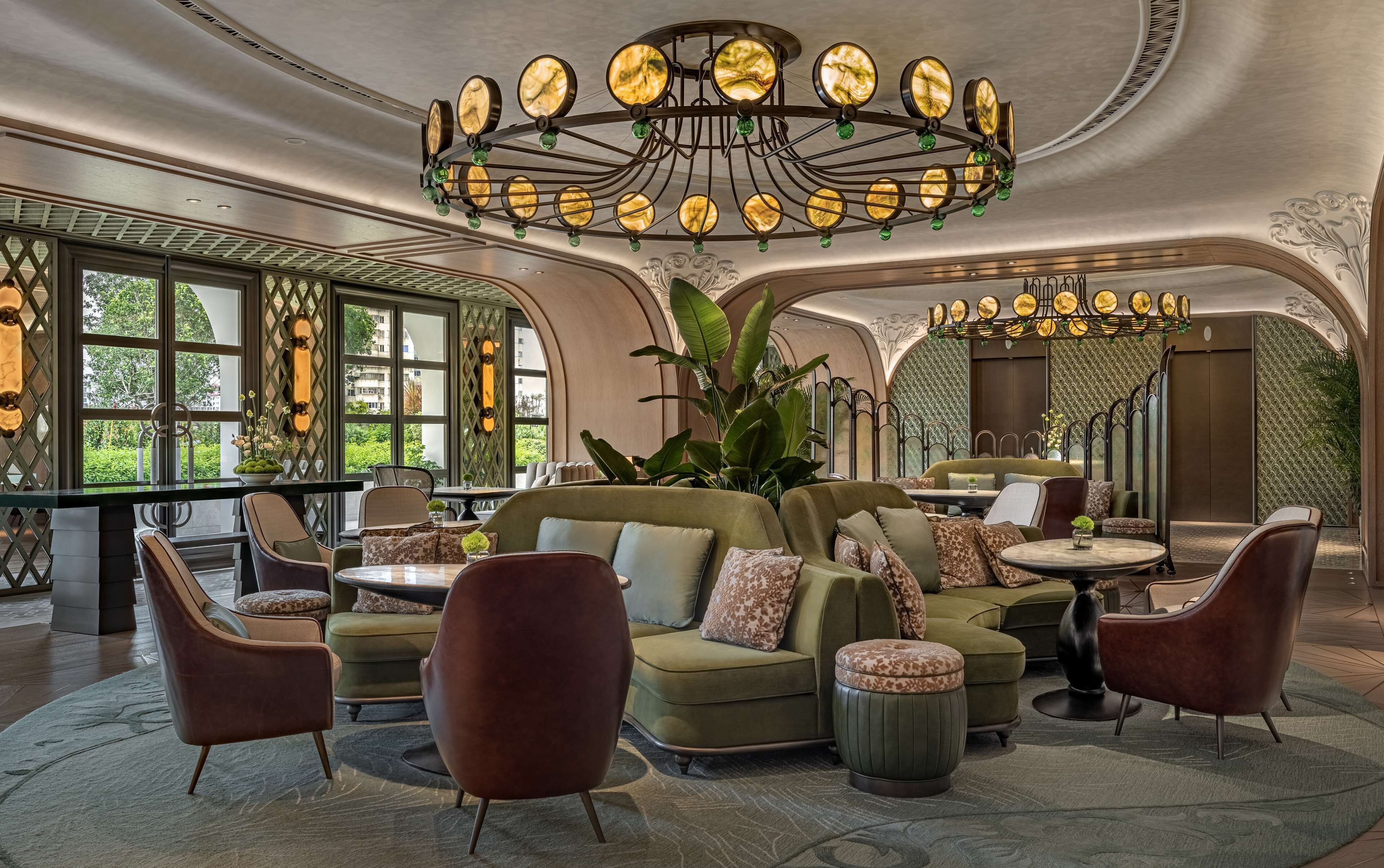 A luxurious interior with a central seating area, ornate ceiling, and large windows offering a view of greenery.