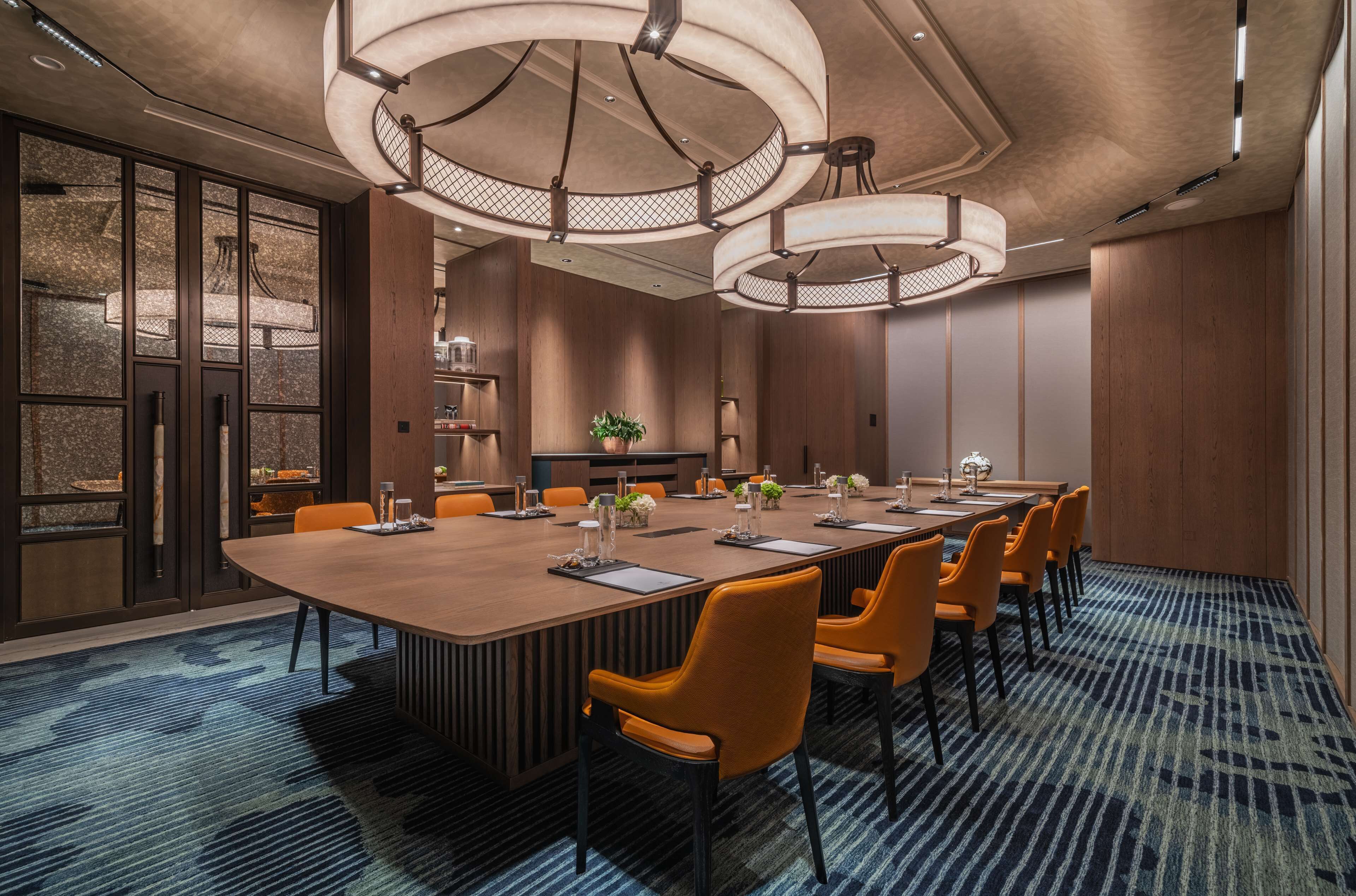 Une salle de conférence dotée d’une longue table, de chaises orange et de luminaires modernes.