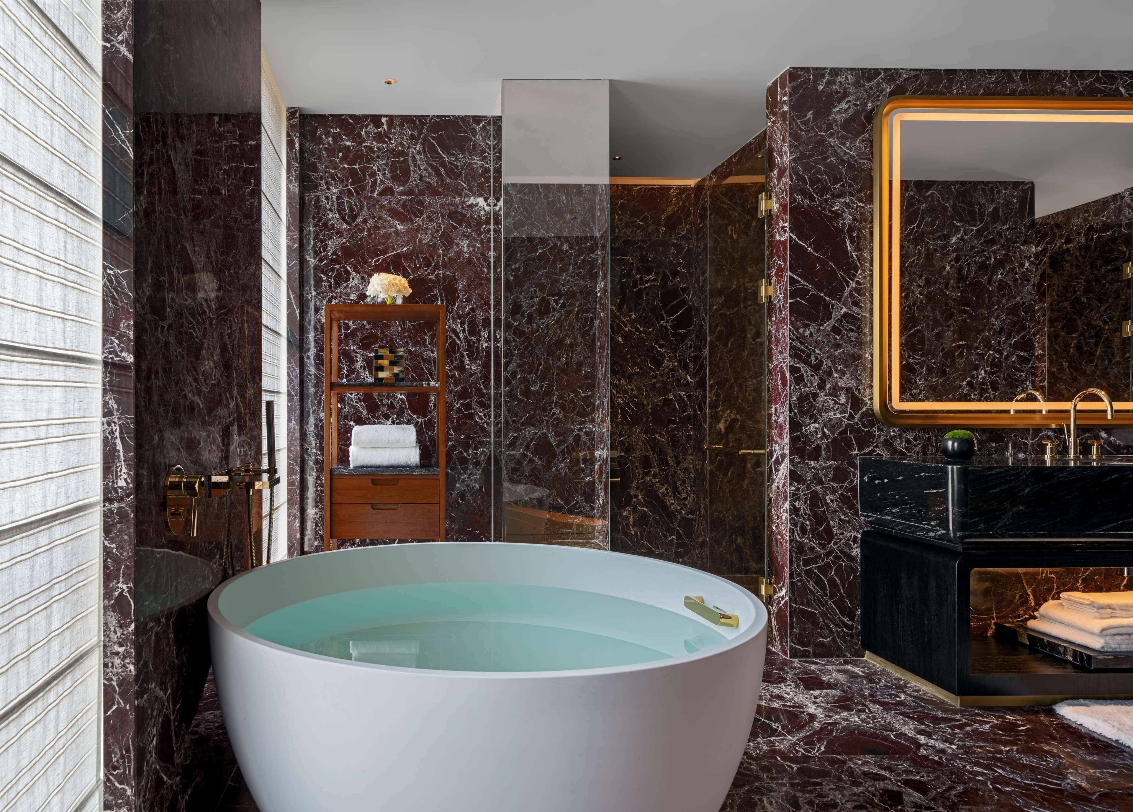 Un baño moderno con una bañera independiente grande, ducha con cerramiento de vidrio y tocador con espejo de marco dorado.
