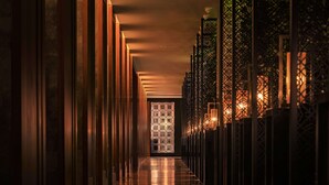 Un couloir dont le mur du fond est orné d’un motif, et de part et d’autre duquel se trouvent des luminaires verticaux.