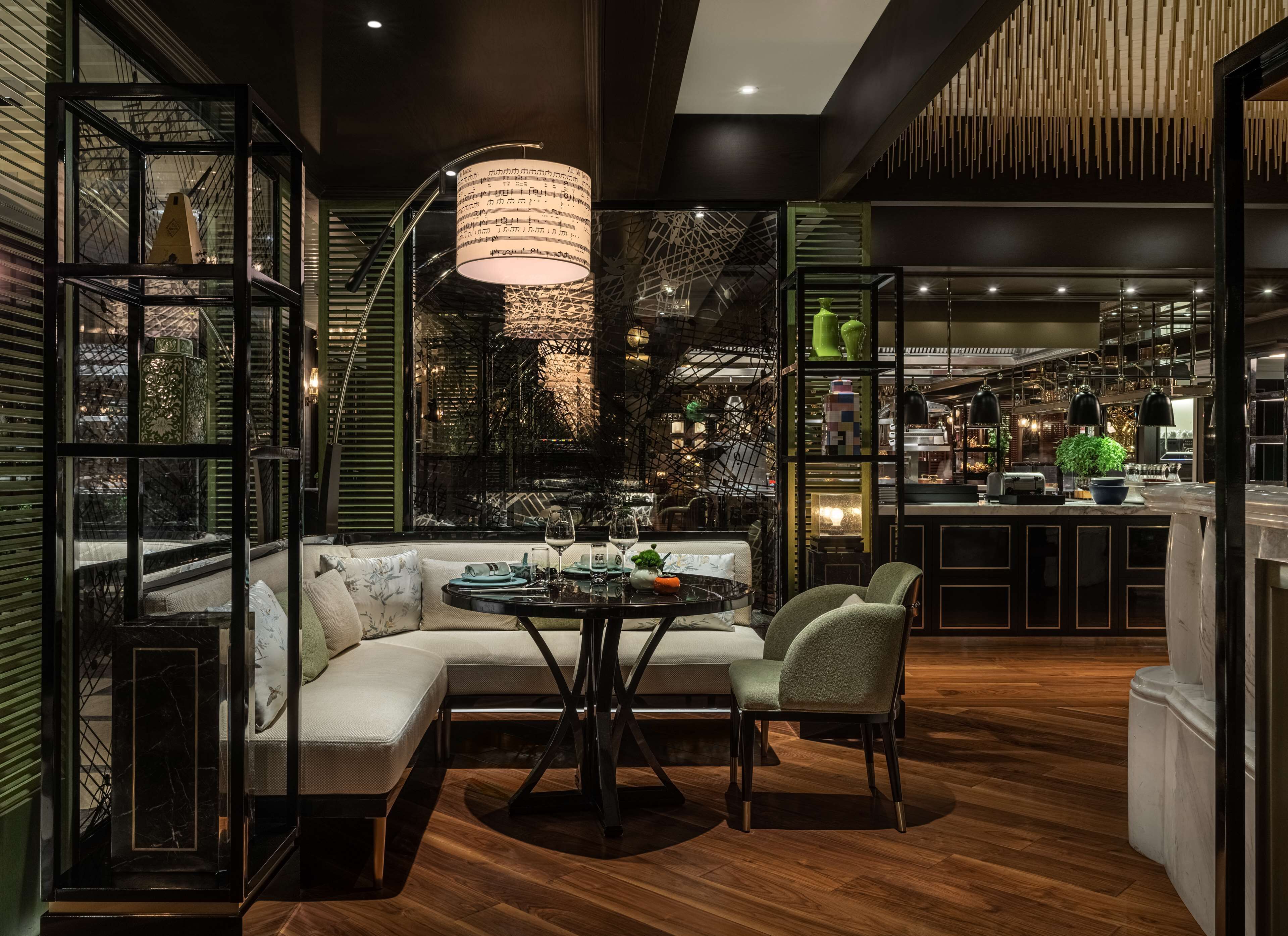 Un interior moderno con un sofá modular, una mesa redonda y sillas, rodeado por separadores de vidrio y una lámpara colgante decorativa.