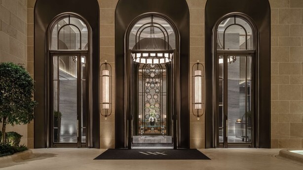Une entrée imposante, dotée de trois portes cintrées, chacune étant munie d’une porte en verre et d’un luminaire fixé au mur.