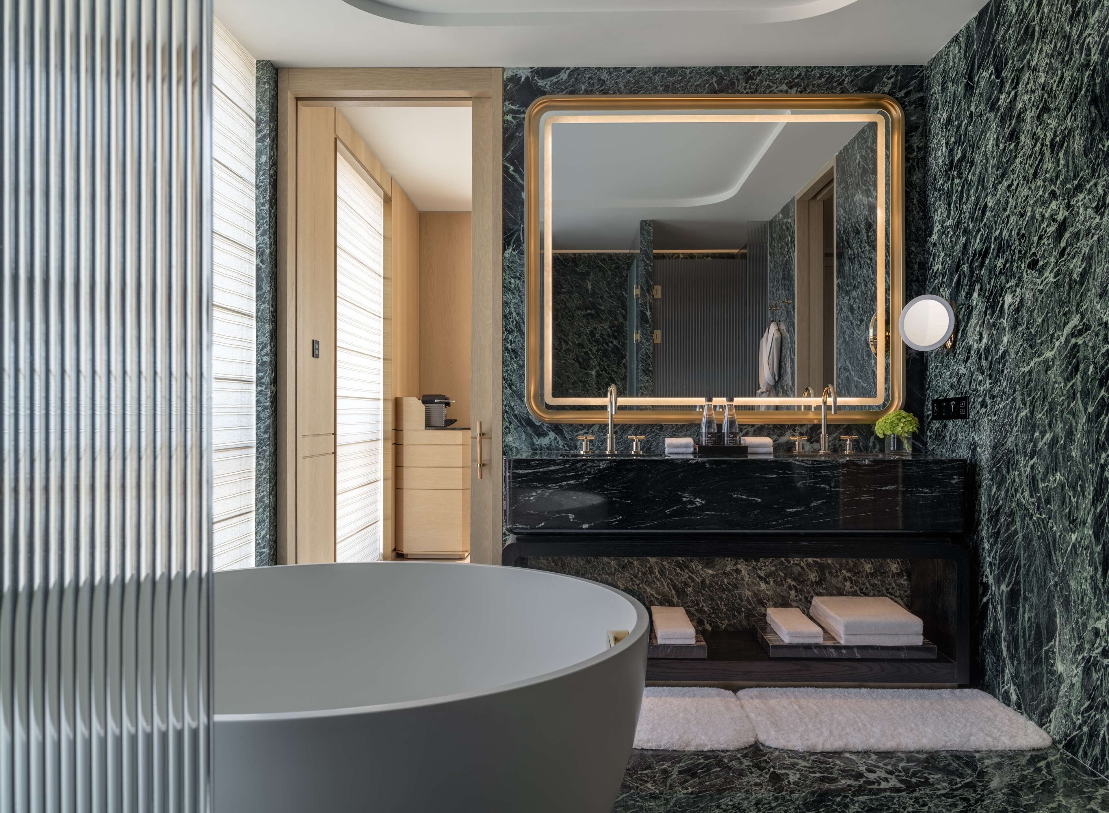 Une salle de bain moderne dotée d’une grande baignoire, d’un meuble-lavabo avec un plan de travail en marbre et d’un grand miroir avec un cadre doré.