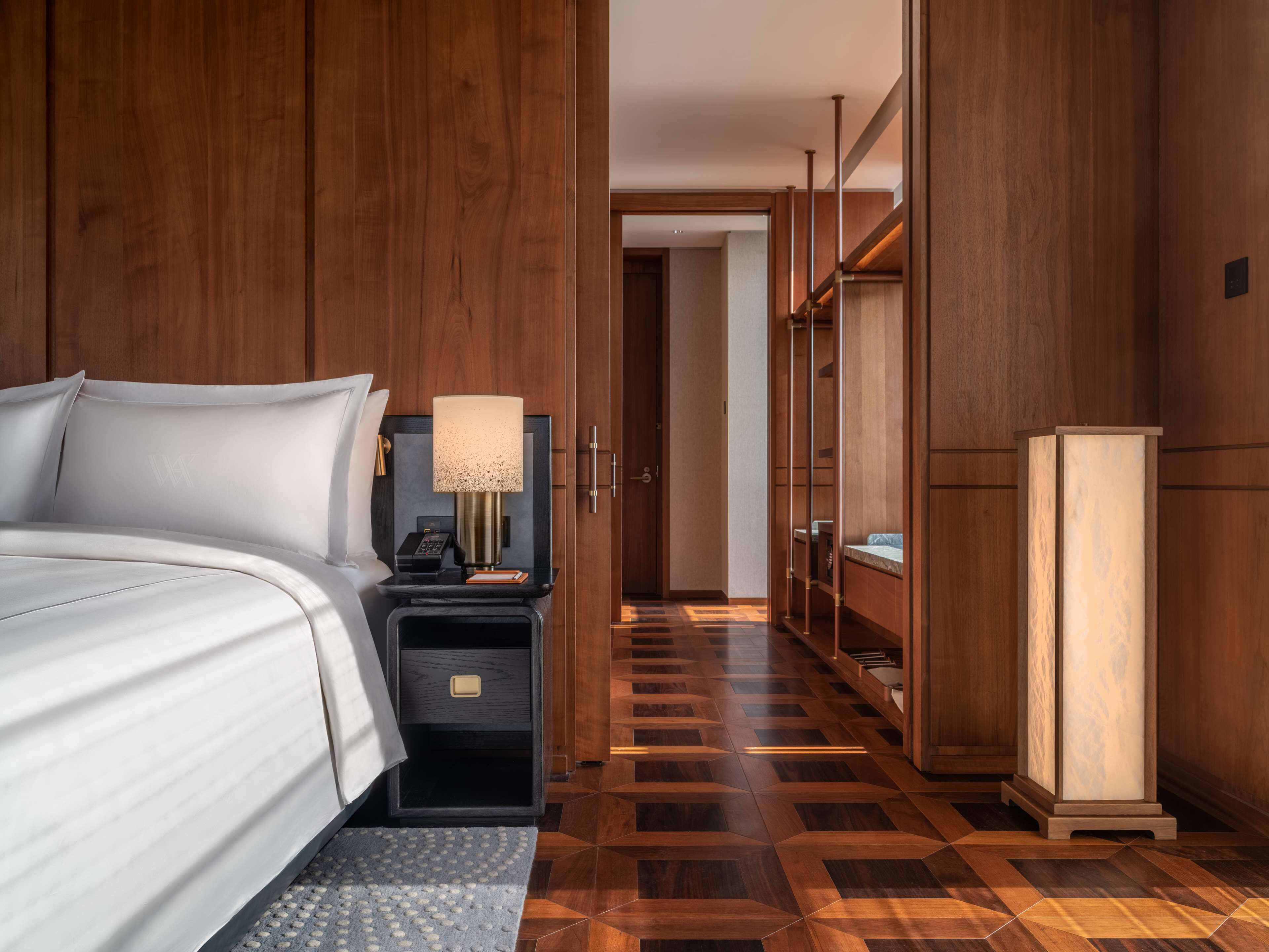 Een hotelkamer met een bed, nachtkastje met lamp, kast en spiegel.
