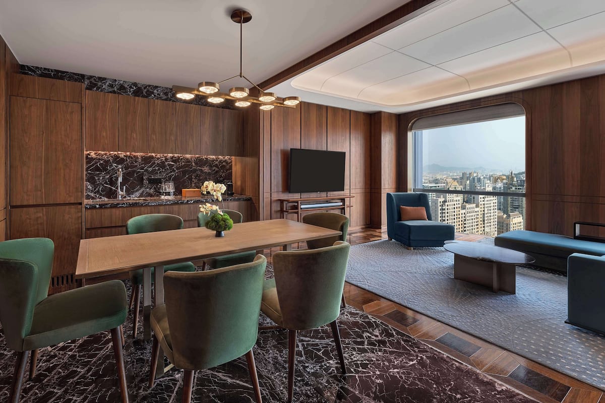 Ein modernes Wohnzimmer mit Essbereich, einem großen Fenster und Blick auf die Stadt sowie einem an der Wand befestigten Flachbildfernseher.