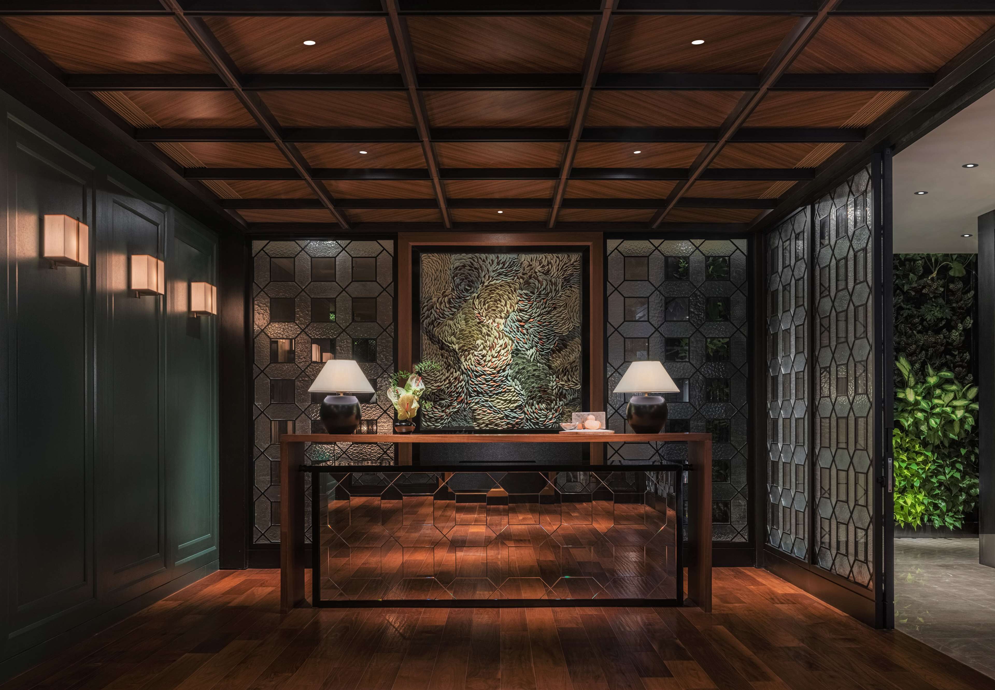 A reception area with a wooden reception desk, two wall-mounted lamps, and a hexagonal patterned wall.