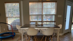 Un espace repas avec une table et des chaises, un trampoline et de grandes fenêtres équipées de stores.