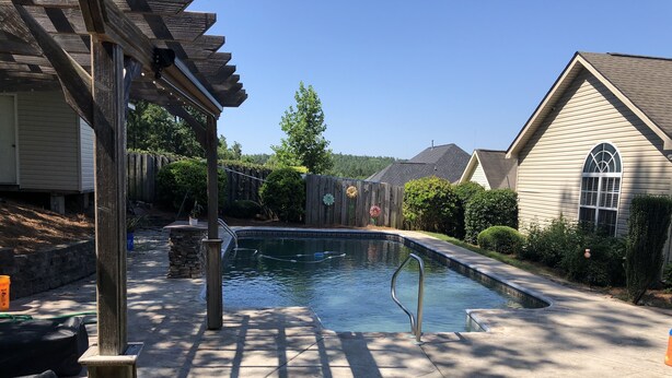 Une piscine résidentielle dotée d’une terrasse en bois, d’une pergola et d’un mur en pierre.