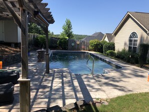 A residential swimming pool with a wooden deck, a pergola, and a stone wall. - Masters & LPGA 2020 Rental (North Augusta)