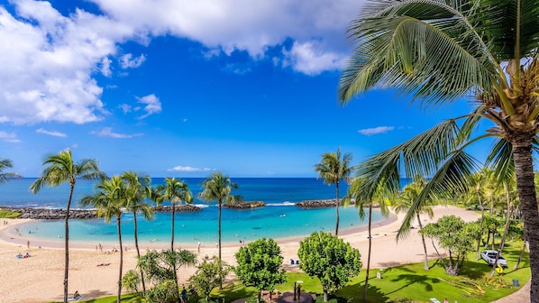 Une plage à l’eau d’un bleu cristallin, bordée de palmiers et d’une côte rocheuse.