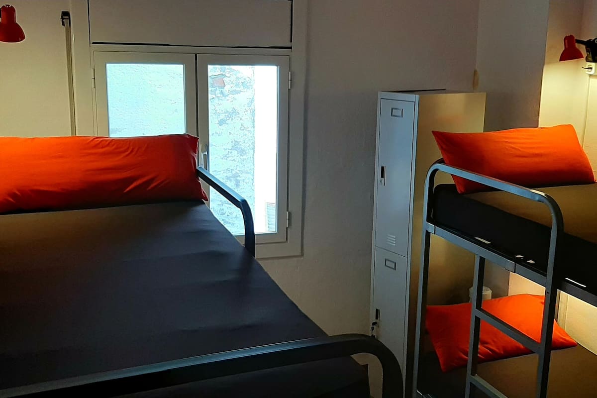 Habitación tipo dormitorio con dos literas, cada una con una almohada naranja, un escritorio y una ventana.