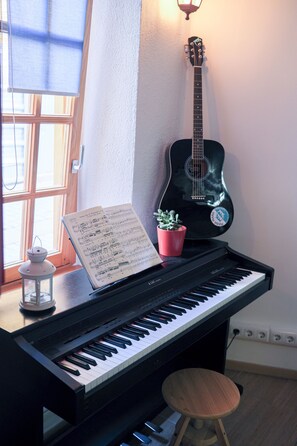 Un piano con partituras, una guitarra, una pequeña planta en maceta y un taburete.