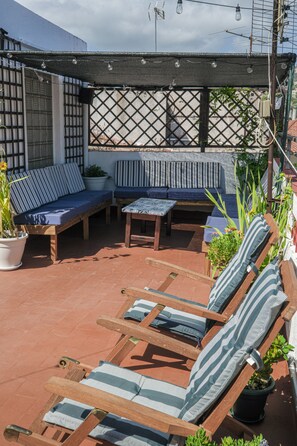 A patio with wooden furniture, including a sofa and lounge chairs, and potted plants. - Mana Mana Youth Hostel (Tossa de Mar)
