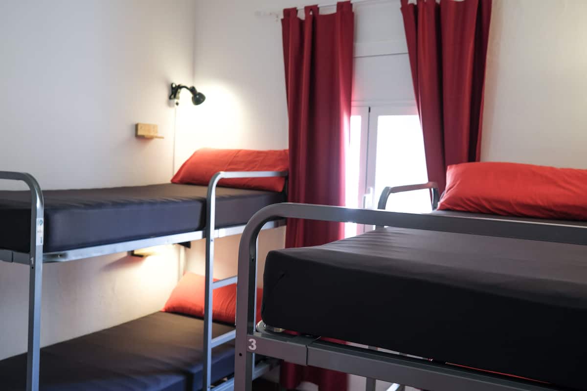Dormitorio con literas, cortinas rojas y una lámpara fijada a la pared.