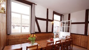 A dining area with a wooden table and chairs, a vase of tulips, and a window with curtains.