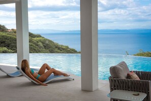 A woman relaxing by a pool with a view of the sea and mountains. - Ocean-View Luxury Villa – All-Inclusive with Helipad, Gym & Chauffeur (Playa Ocotal)