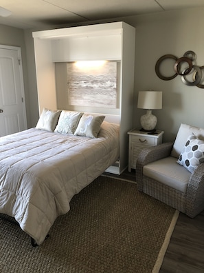 Een slaapkamer met een groot bed, een kleine bank, een nachtkastje, een lamp en een kunstwerk aan de muur.