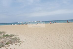 A beach with sun loungers and umbrellas, a clear sky, and the ocean in the background. - Apartment 50m from the sandy beach with communal pool in Denia, km 3 (Dénia)