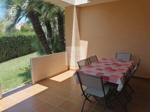 A balcony with a table and chairs, a view of a garden with palm trees, and a building in the background. - Apartment 50m from the sandy beach with communal pool in Denia, km 3 (Dénia)