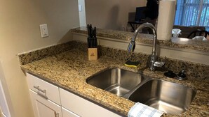 Una cocina con encimeras de granito, pileta de acero inoxidable y muebles de color blanco.