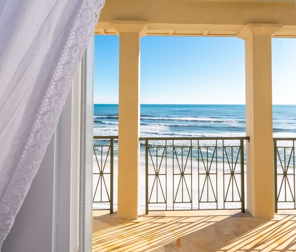 A balcony with a view of the ocean, a railing, and a wooden floor.