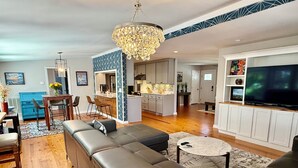 A modern living room with a sectional sofa, a dining area with chairs, a kitchen, and a TV. - The Perfect Relaxing Oasis for your family’s Island Getaway (Isle of Palms)