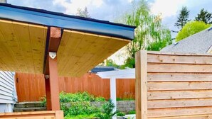Une porte en bois mène à une zone pavée, bordée d’un mur en pierre et agrémentée de plantes en pot.